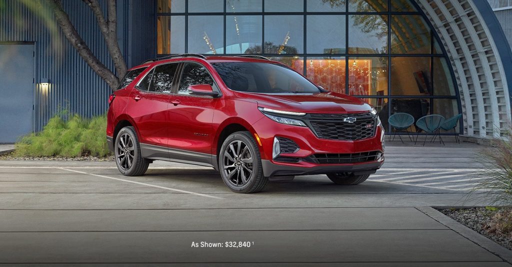 An all-new 2024 Radiant Red Tintcoat Chevy Equinox parked in front of a modern shop in McGregor, TX.