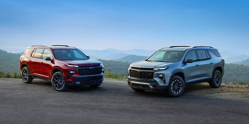 Two all new 2024 Chevy Traverse SUVs parked at a vantage point with rolling forested hills in the backdrop. - Jim Turner Chevrolet McGregor, TX 