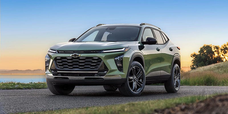 An all-new 2024 Cacti Green Chevy Trax parked on a paved side road with trees, hills, and water in the back drop. - Jim Turner Chevrolet McGregor, TX