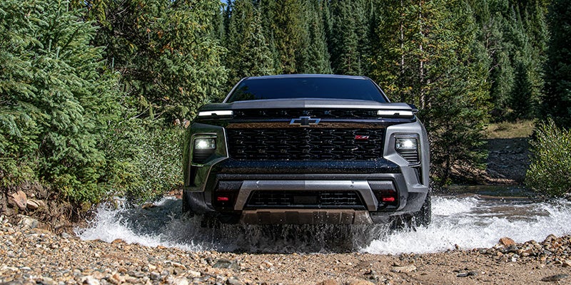 A 2024 Gray Chevrolet Traverse Limited facing directly straight on to the camera driving through a stream in the wooded hills. - Jim Turner Chevrolet McGregor, TX