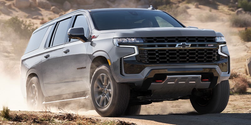 An all-new Gray 2024 Chevrolet Suburban driving on a dusty back road. - Jim Turner Chevrolet McGregor, TX