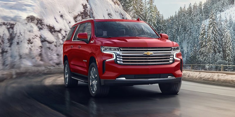 An all-new Red 2024 Chevy Suburban driving on a snow covered mountain highway. - Jim Turner Chevrolet McGregor, tX