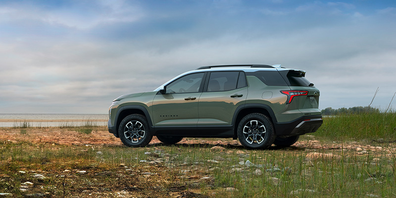 An all-new forest green 2025 Chevy Equinox parked in a grassy beach in front of a body of water. - Jim Turner Chevrolet McGregor, TX